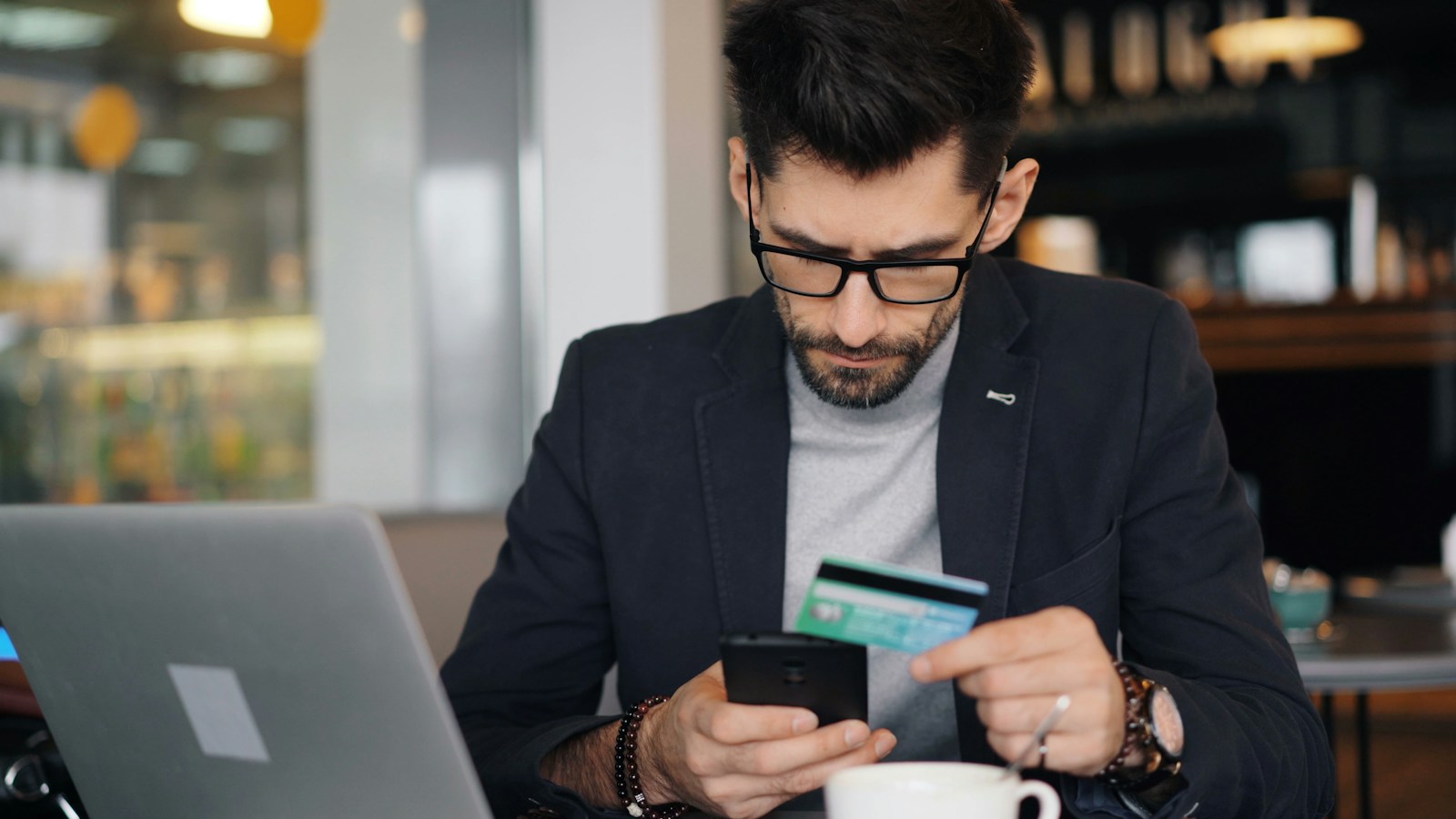 Homem confere o cartão de crédito e o celular para negociar anuidade