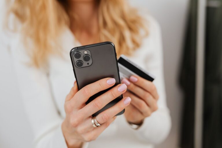 Mulher compara pontos ou cashback no celular com o cartão na mão