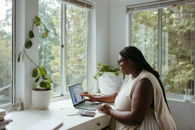 Mulher organizando a renda extra em casa com notebook e calculadora