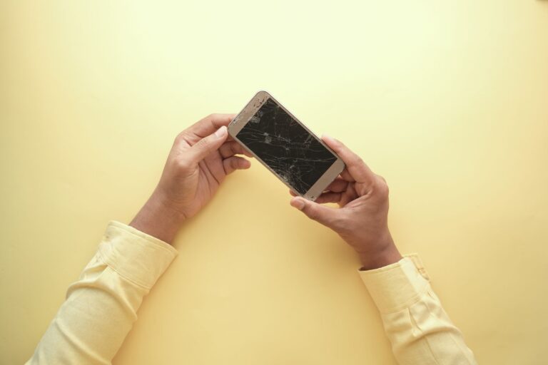 Mãos segurando um celular com a tela quebrada, tema do seguro de celular