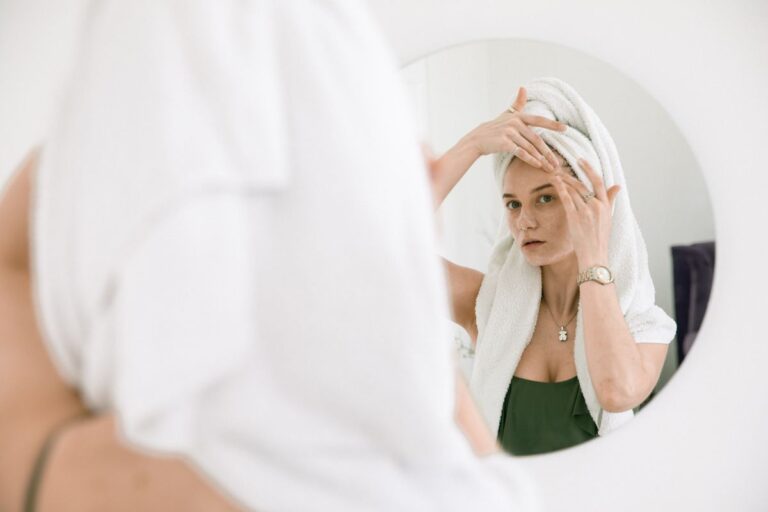 Mulher aplicando creme no rosto diante do espelho, em um skincare noturno
