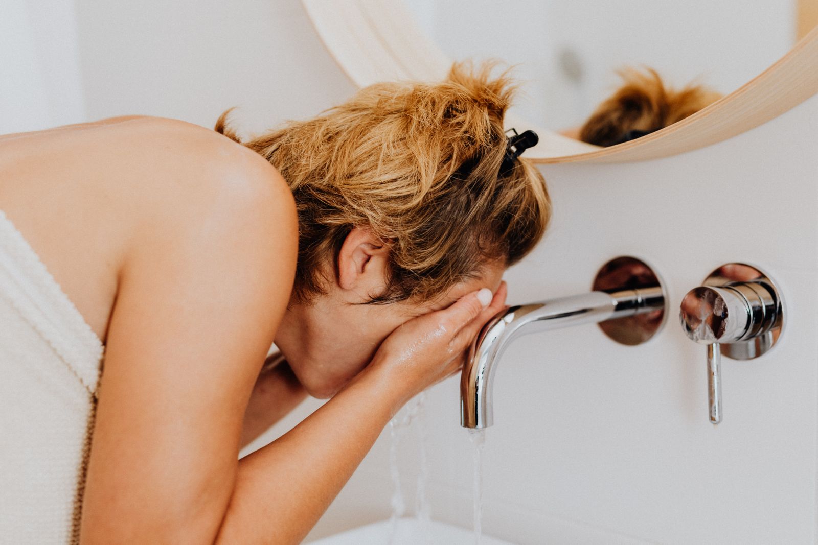 Mulher lavando o rosto na pia, primeiro passo do skincare para pele oleosa